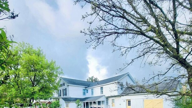 Ein zweistöckiges Haus mit überdachter Veranda und einem gepflegten Rasen.