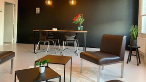 Een moderne wachtruimte met een zwarte muur, een houten tafel, twee stoelen, een bruine lederen fauteuil, een klein tafeltje met een plant en hanglampen.