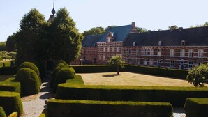 Een formele tuin met geometrisch gesnoeide hagen en een bakstenen gebouw met een flauw hellend dak.