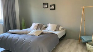 Een slaapkamer met een bed, grijs beddengoed, een grijze muur en twee ingelijste foto’s.