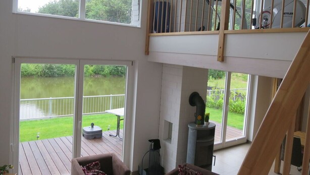 A spacious loft with a balcony, a fireplace, and a view of a lake.