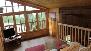 A wooden cabin interior with a TV, wicker furniture, and large windows offering a view of the outdoors. - Wiesbachhutte Mountain hut (Reichenau)