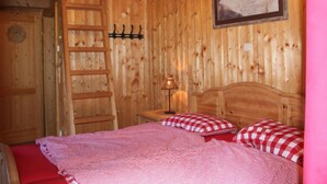A wooden room with a bed, a ladder, a wall-mounted coat rack, and a painting. - Wiesbachhutte Mountain hut (Reichenau)