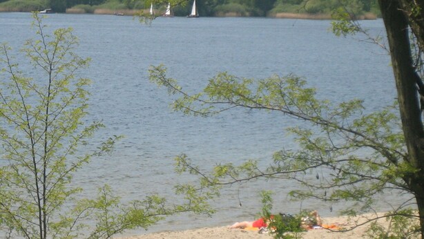 Un lac où voguent des voiliers, une plage de sable et des arbres au premier plan.