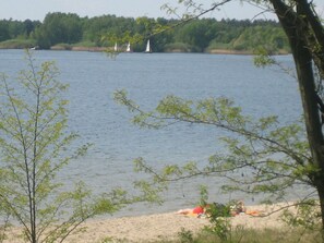 A lake with sailboats, a sandy beach, and trees in the foreground. - Apartment on the Beach With sea View (Lohsa)