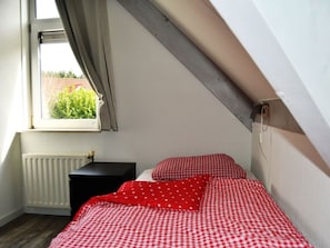 A small, cozy bedroom with a window, a radiator, and a bed with red checkered bedding. - Noordzeeboulevard 51 (Kamperland)