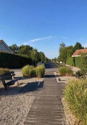 A wooden pathway leading through a landscaped area with benches and greenery. - Noordzeeboulevard 51 (Kamperland)