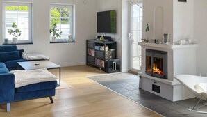 Un salon moderne avec un canapé bleu, une cheminée, un téléviseur et une bibliothèque.