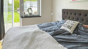 Une chambre à coucher avec un lit, une fenêtre, une plante et une étagère fixée au mur, sur laquelle est posé un panneau.