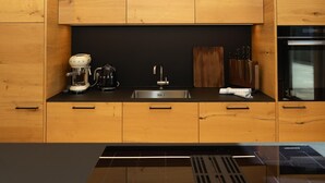 Una cocina moderna con armarios de madera, cafetera, hervidor, pileta y horno empotrado.