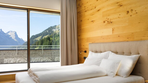 Un dormitorio con un ventanal grande, paredes de madera y una cama con ropa blanca.