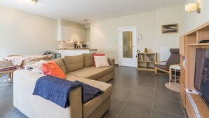 Ein modernes Wohnzimmer mit einer Couch, einem Fernseher und einem Essbereich mit Tisch und Stühlen.