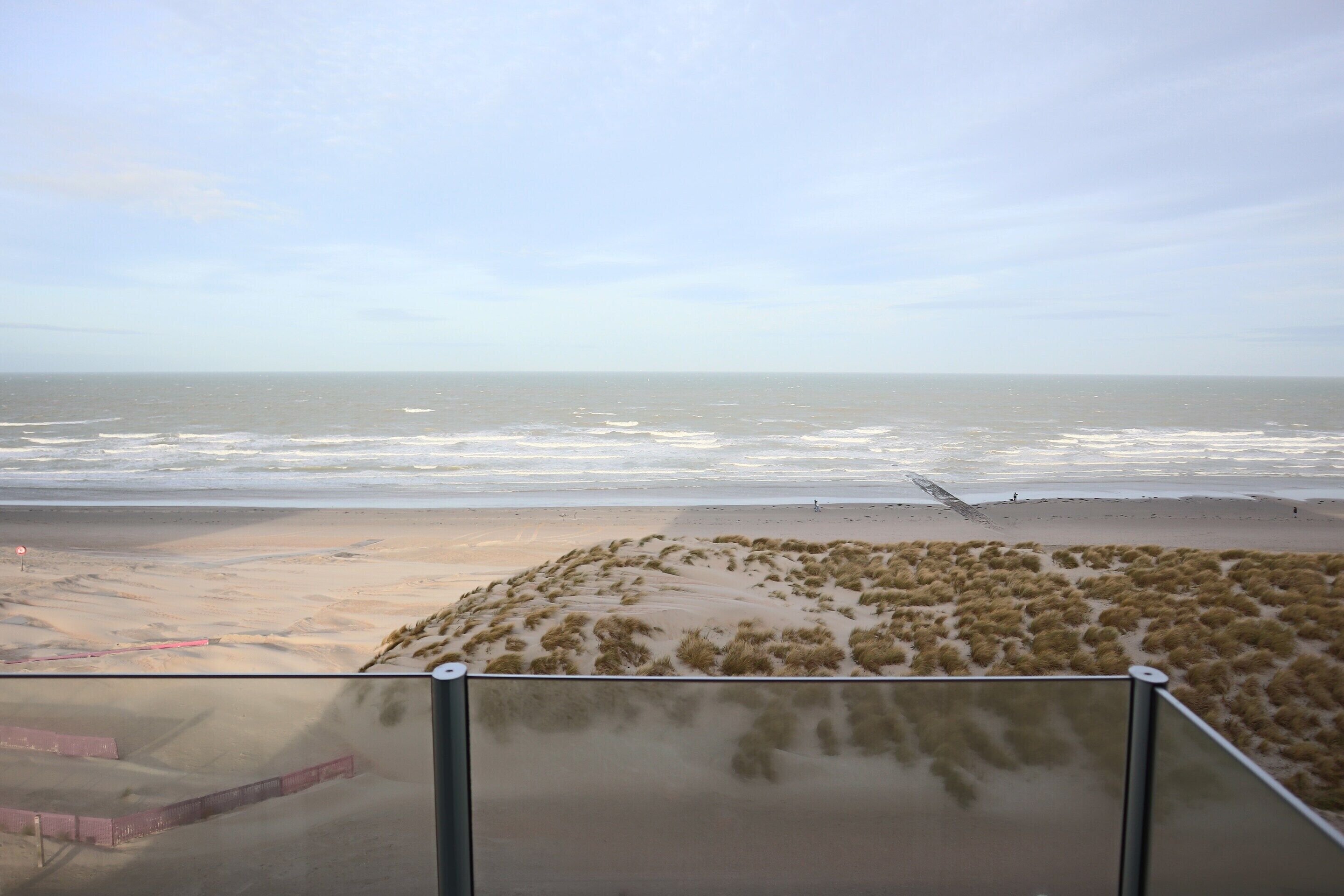 A beach view from a balcony with sand dunes and a clear sky.