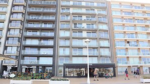 A multi-story hotel with balconies, a central entrance, and a parking area with bicycles. - Coastal Comfort by the Sea (Nieuwpoort)