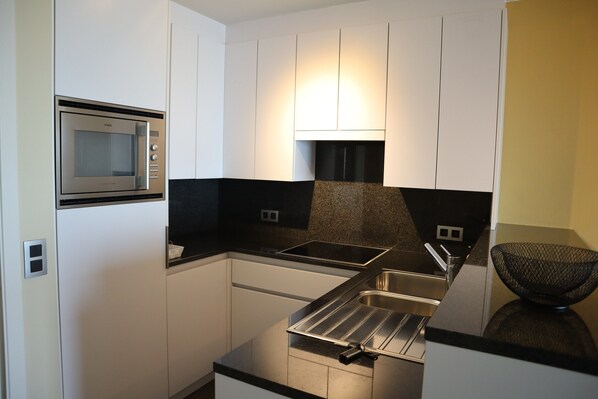 A modern kitchen with white cabinets, a stainless steel microwave, a black countertop, and a black sink. - Coastal Comfort by the Sea (Nieuwpoort)
