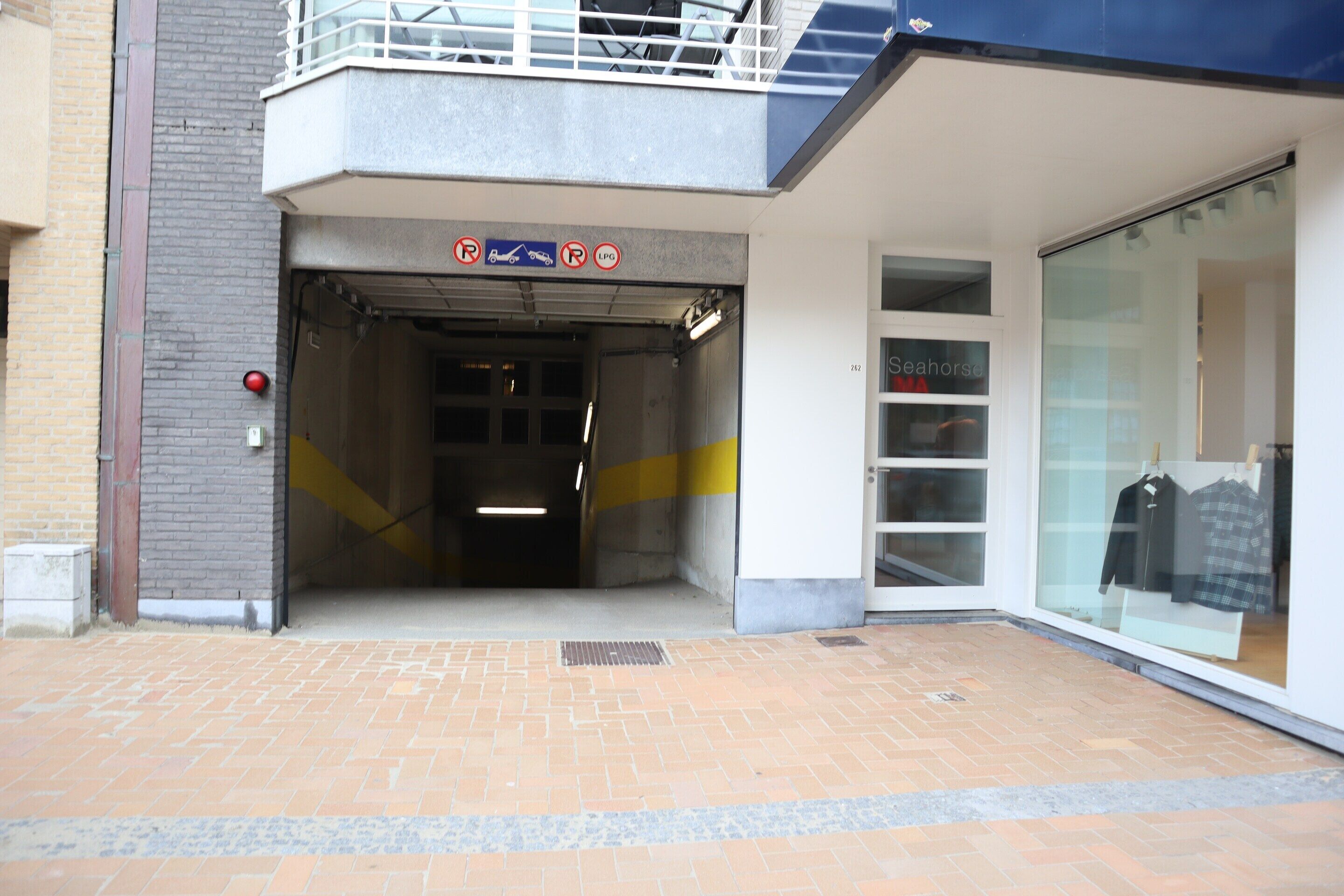 A building entrance with a garage door, a sign indicating parking restrictions, and a storefront with clothing items on display.