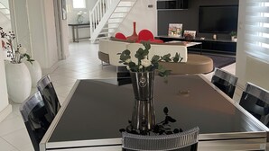 Un salon moderne avec un coin repas, comprenant un escalier, un canapé, un téléviseur et des vases décoratifs.