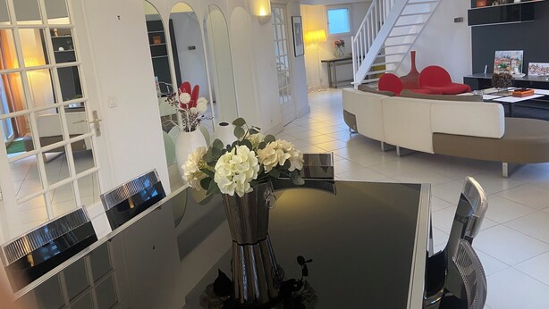 Un salon moderne avec un coin repas, des murs blancs et un escalier menant à un niveau supérieur.