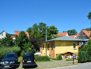Ein gelbes Gebäude mit einem grünen Dach, umgeben von Bäumen und anderen Häusern.
