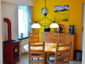 Ein Essbereich mit einem runden Tisch, Holzstühlen, einem roten Herd, einer Uhr und einem Gemälde an der Wand.
