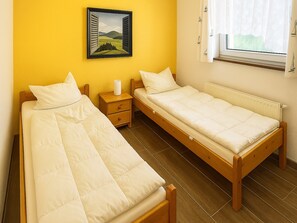 Ein Zimmer mit zwei Einzelbetten, einem Nachttisch mit Lampe, einem Fenster mit Ausblick und einem Bild an der Wand.