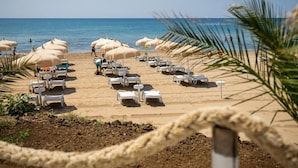 A beach with rows of white lounge chairs and beige umbrellas, a clear blue sky, and the ocean in the background. - Apartment With Garden or Terrace Near sea (Isola di Capo Rizzuto)