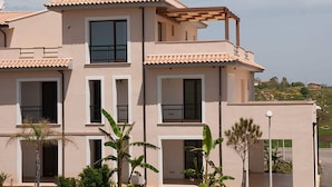 A multi-story residential building with a flat roof, balconies, and a garden area with palm trees. - Apartment With Garden or Terrace Near sea (Isola di Capo Rizzuto)