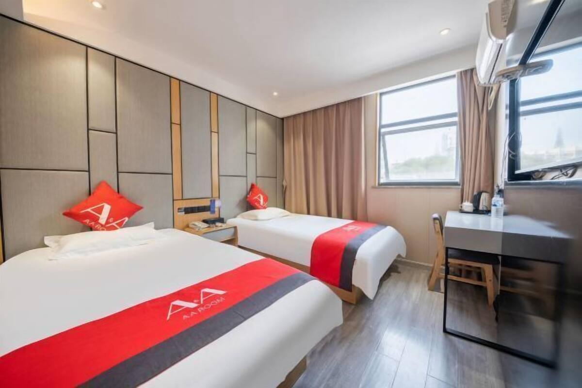 A hotel room with two beds, a desk, and a window.