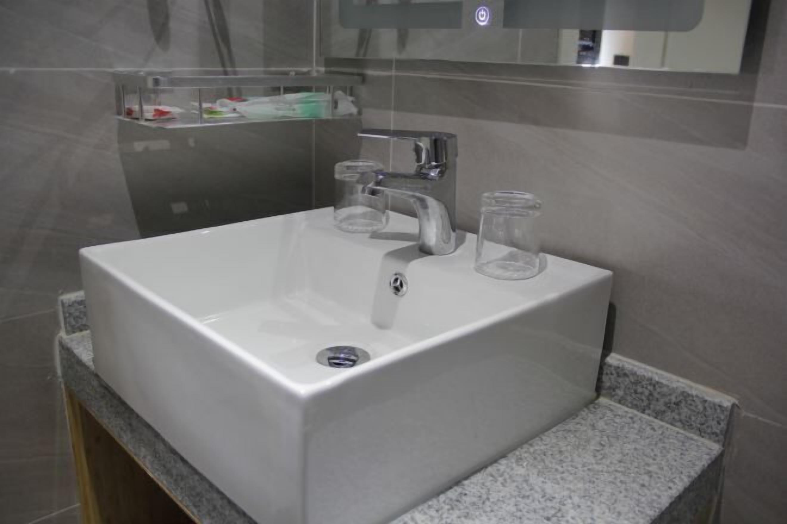 Une salle de bain moderne avec un lavabo blanc, un miroir au-dessus et une étagère en verre où sont rangés les articles de toilette.