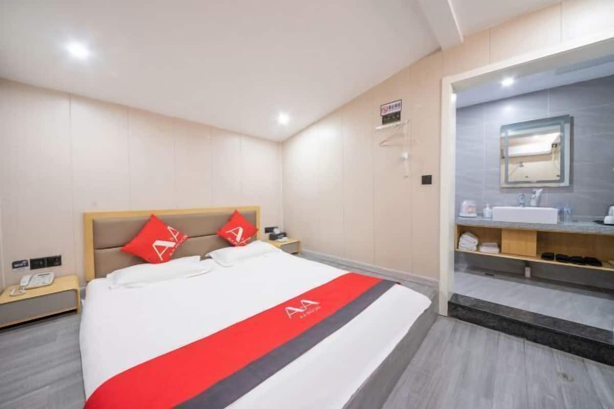 A hotel room with a bed, a nightstand, a red and white bedspread, a bathroom with a mirror, and a towel rack.