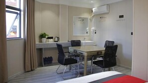 A compact hotel room with a kitchenette, a dining area with two chairs, a bed, a window with curtains, and a small plant. - AA Hotel Chain (Quzhou International Financial Center Shuiting Branch) (Quzhou)