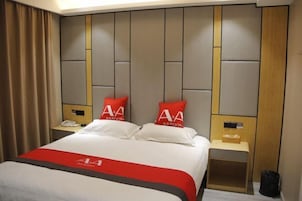 Una habitación de hotel con una cama grande, dos mesitas de noche, un teléfono y una pequeña mesa de madera con un cesto de basura.