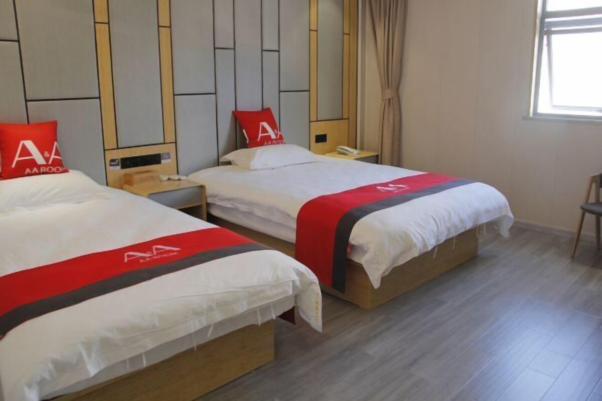 Ett hotellrum med två sängar, var och en med ett rött och vitt sängöverkast, ett träfärgat sänggavel och ett nattduksbord med en telefon, samt ett fönster med gardiner.