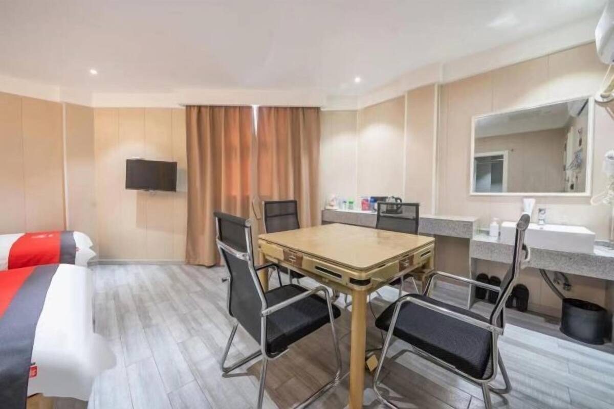 A hotel room with a bed, a dining table with chairs, a TV mounted on the wall, and a bathroom with a mirror and sink.