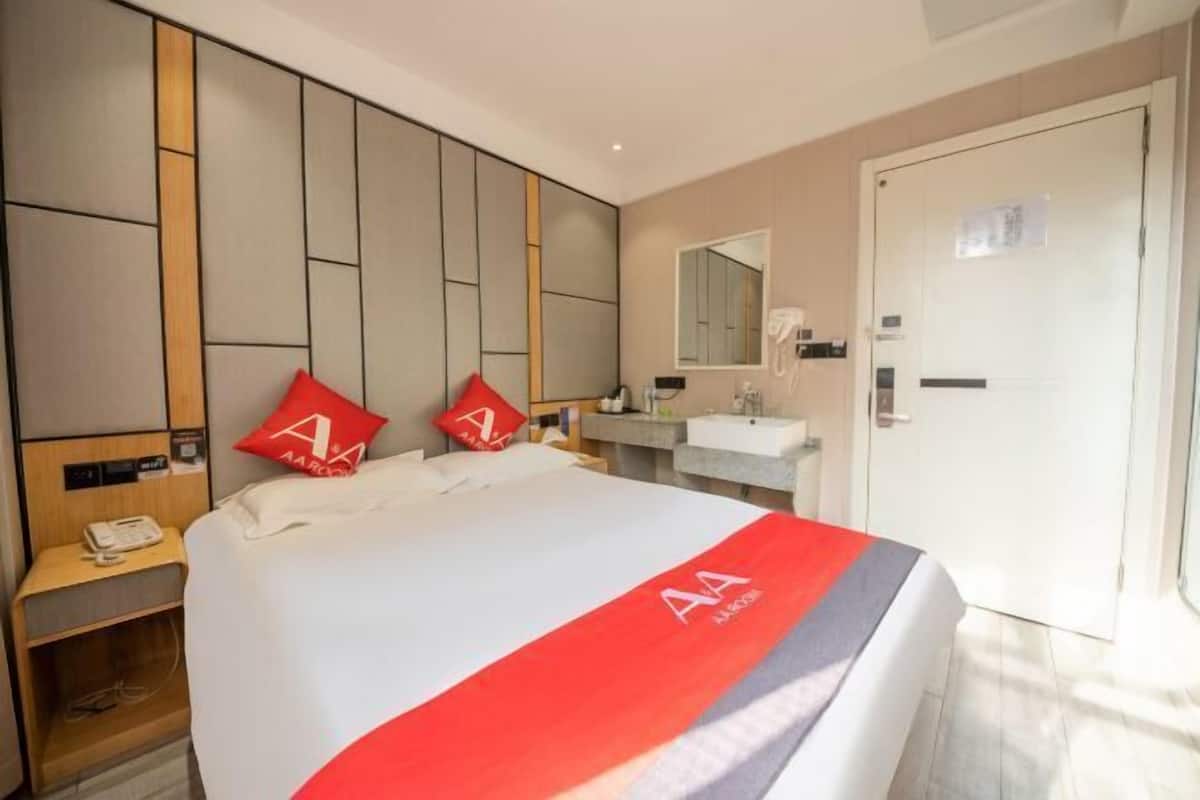 A hotel room with a bed, a nightstand, a desk, a mirror, and a door.