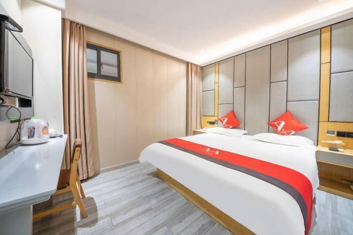 A hotel room with a bed, a desk, a chair, a TV, and a window with curtains.
