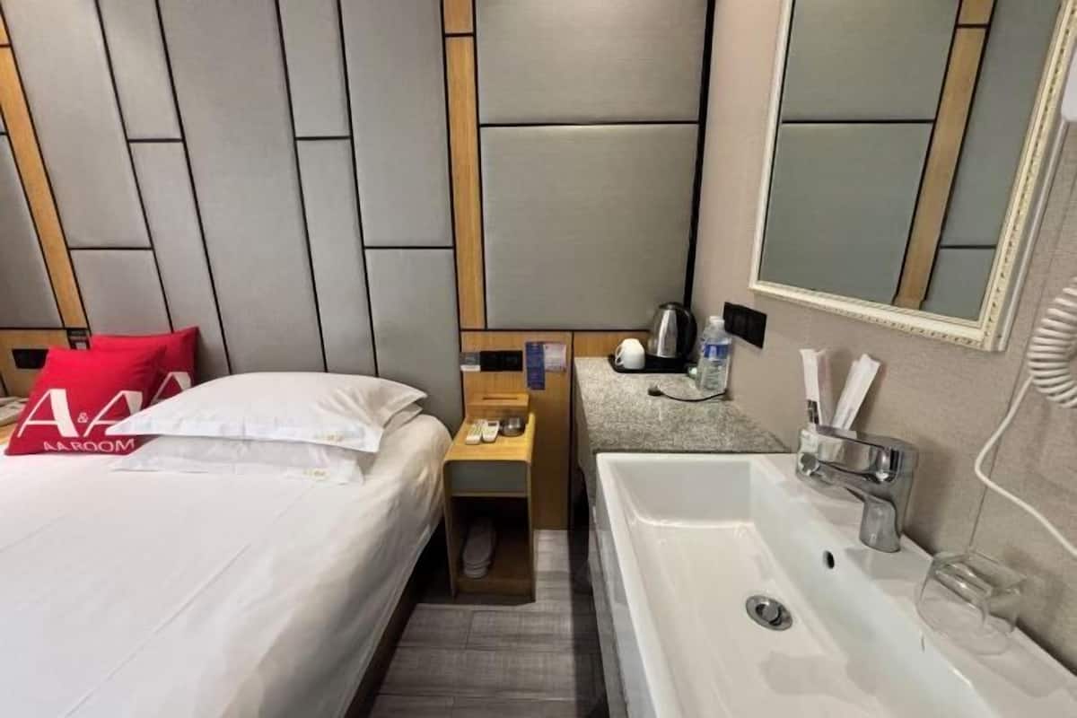 A hotel room with a bed, a nightstand, a sink, and a mirror.