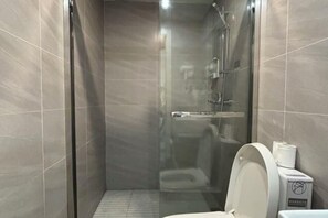 Ett badrum med en dusch som är avskärmad med glasväggar, en toalett och en papperskorg.