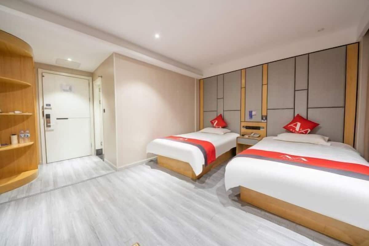 A hotel room with two beds, a wooden wardrobe, and a door leading to another room.