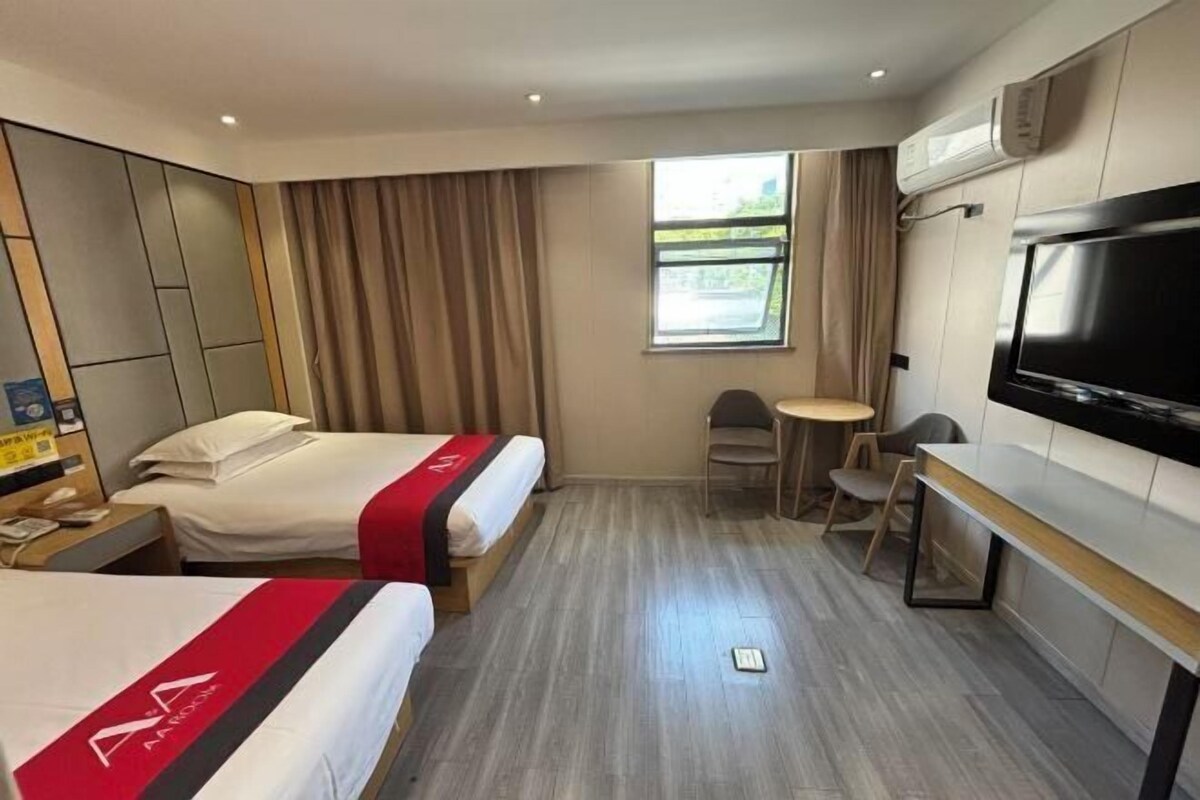 Ett hotellrum med två sängar, en tv, ett litet bord och ett fönster med gardiner.