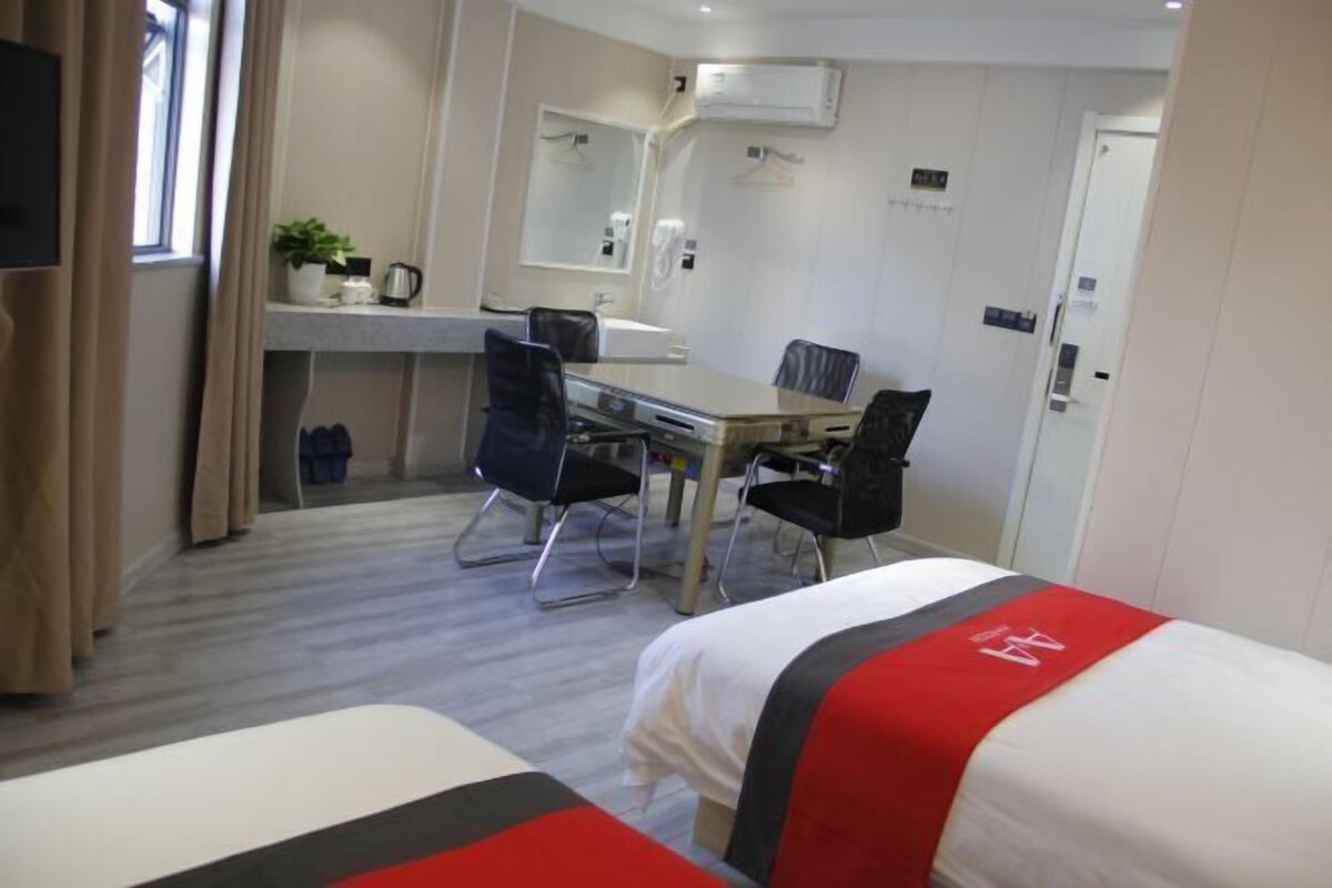 Ett hotellrum med två sängar, ett skrivbord med stolar, en spegel, ett fönster med gardiner och en liten köksvrå.
