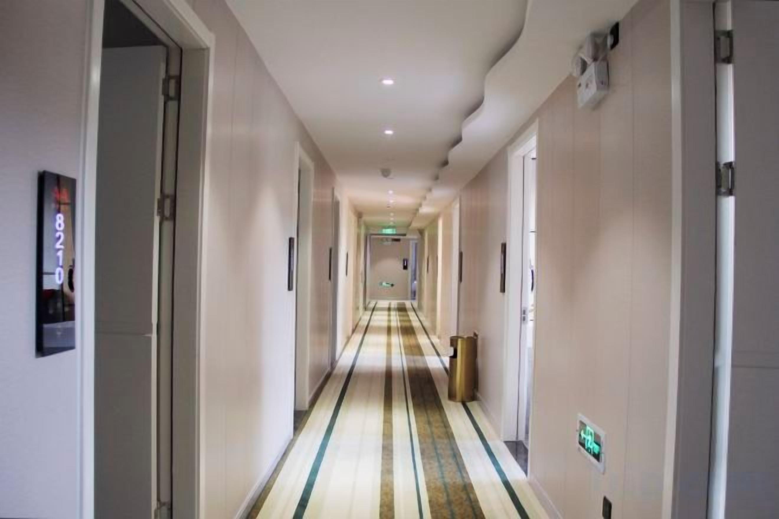 Pasillo de hotel con puertas a ambos lados, alfombra estampada y un cubo de basura en el centro.
