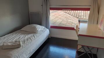 Una habitación pequeña y funcional con una cama individual, un escritorio y una ventana con vistas a un tejado de baldosas.
