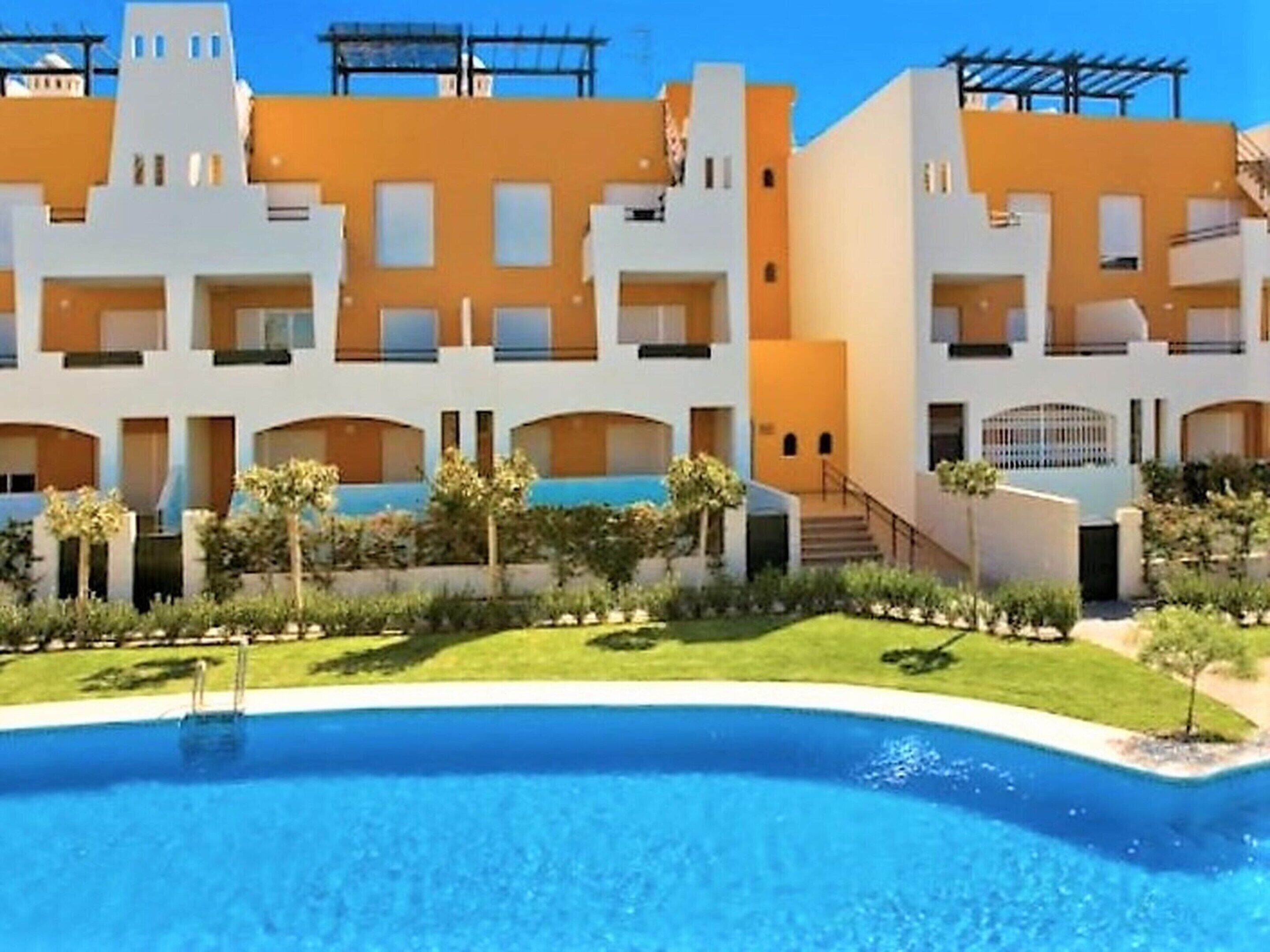 A modern hotel with a pool, multiple balconies, and a well-maintained garden.