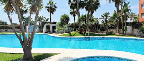 A swimming pool surrounded by palm trees and a small building.