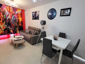 Un salon moderne avec un canapé, une table à manger et des chaises, une lampe et un mur décoré sur le thème des super-héros.