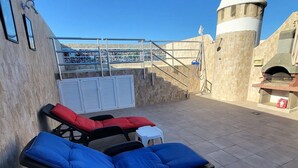 Eine Dachterrasse mit Liegestühlen, einem kleinen Tisch und einer Steinmauer mit einer Treppe zu einer Terrasse.