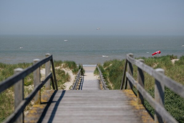 Un escalier en bois mène à une plage où un drapeau rouge est planté sur la droite.