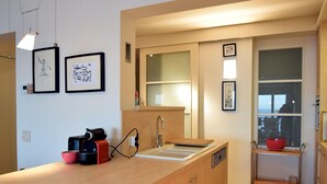 Een moderne keuken met een houten aanrecht, een spoelbak en een kleine trolley. Er hangen afbeeldingen in lijsten aan de muur en een raam met uitzicht.