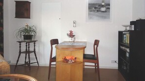 A dining area with a wooden table and chairs, a small side table with a plant, a bookshelf, and a framed picture on the wall. - Time out Zu2! Modern Retreat (Cuxhaven)